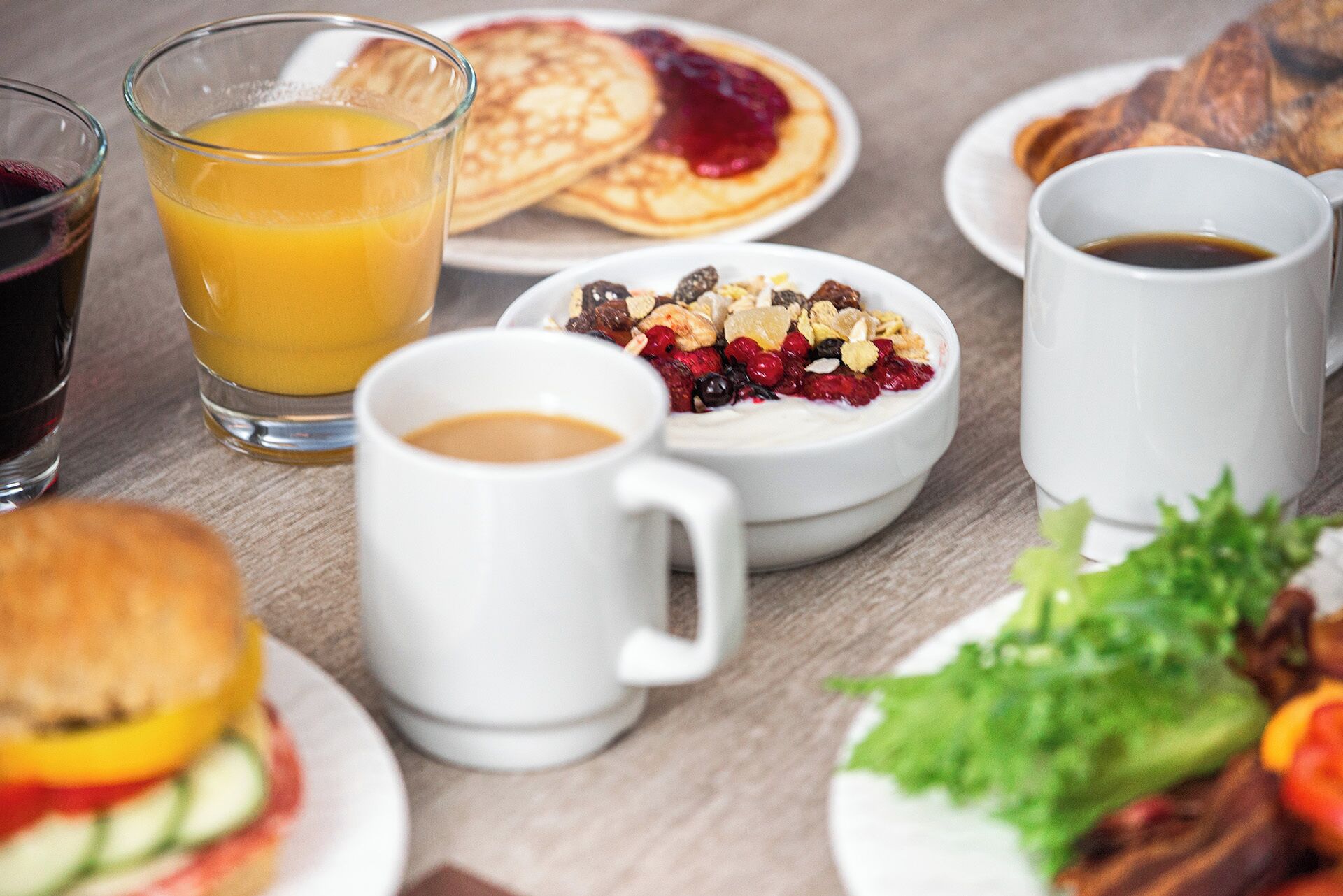 Desayuno con tortitas, zumo de naranja, café, cereales y un sándwich.