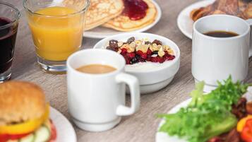 Desayuno con tortitas, zumo de naranja, café, cereales y un sándwich.