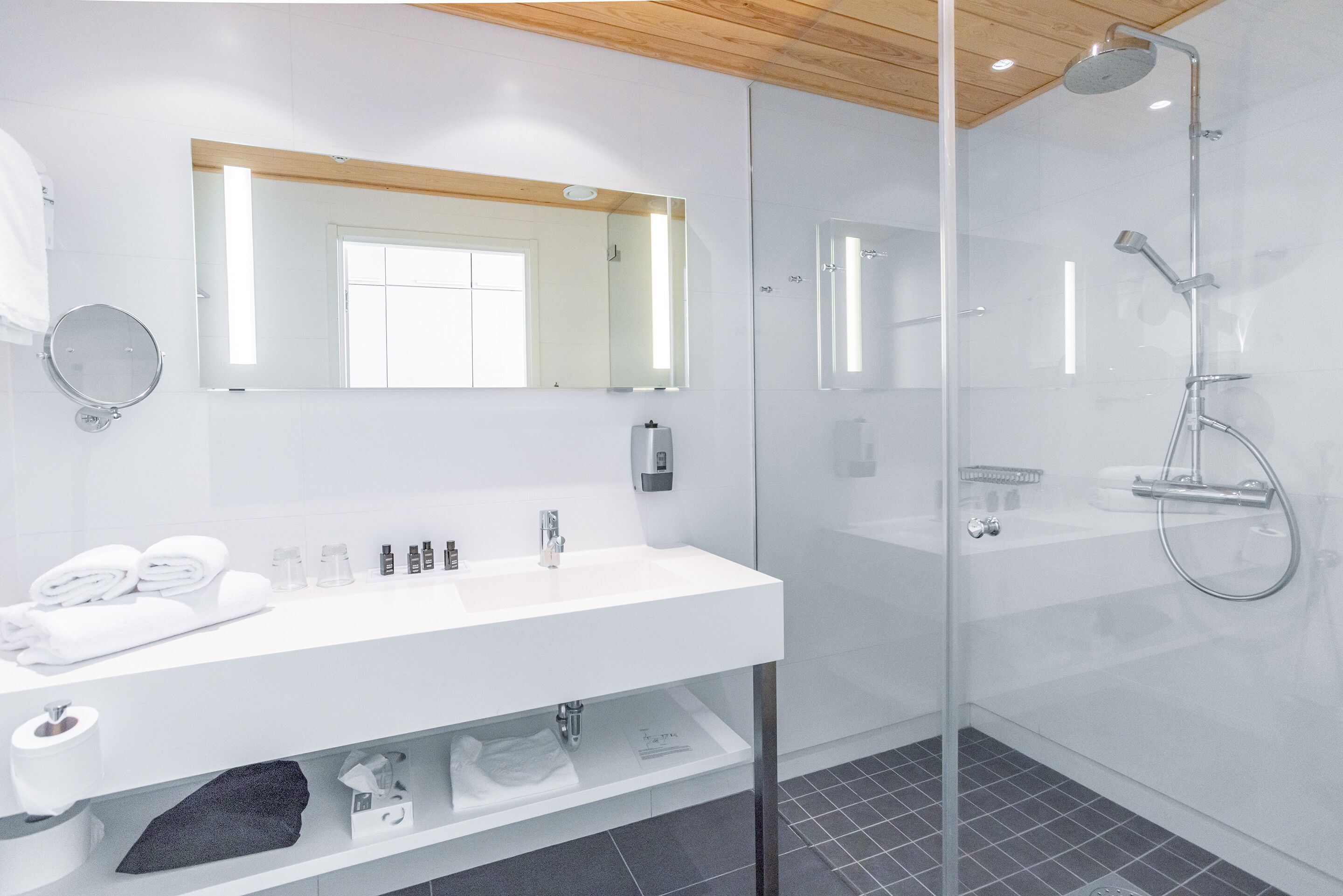 A modern bathroom with a glass-enclosed shower, a white sink with toiletries, and a large mirror.