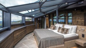 A bedroom with a skylight, wooden walls, a bed with pillows, and a view of the landscape. - Hotel Levi Panorama (Kittila)