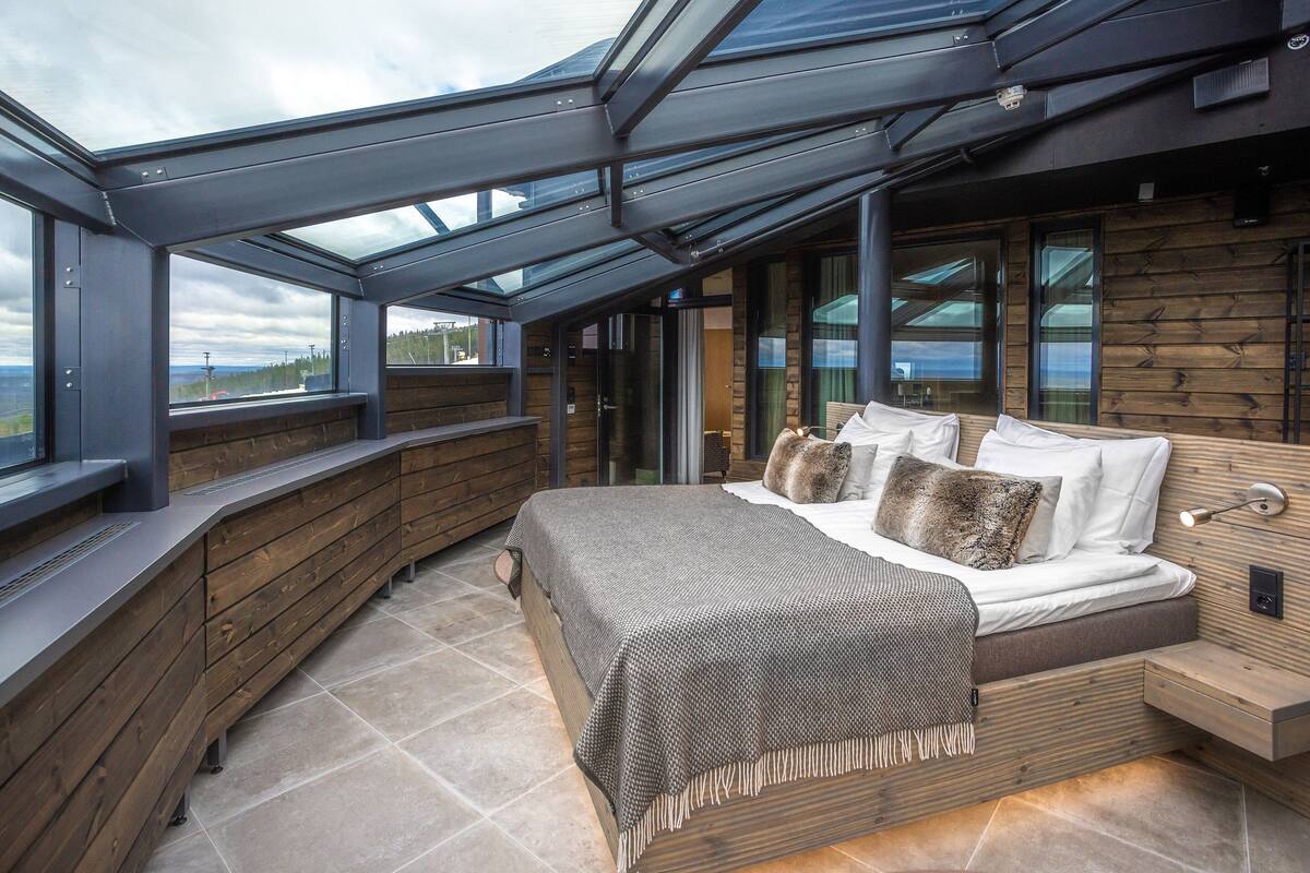 Un dormitorio con tragaluz, paredes de madera, cama con almohadas y vista al paisaje.
