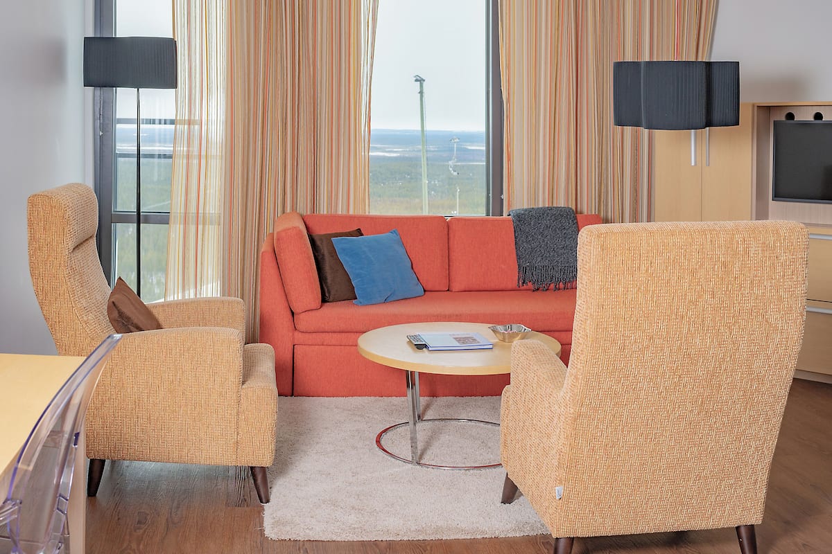 Una sala de estar con un sofá rojo, dos sillones, una mesita redonda y un televisor.