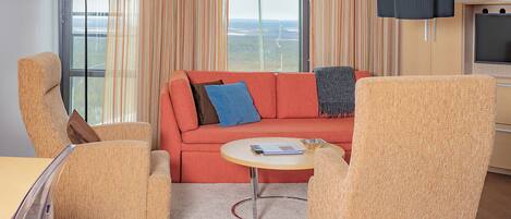 A living room with a red sofa, two armchairs, a small round table, and a TV.