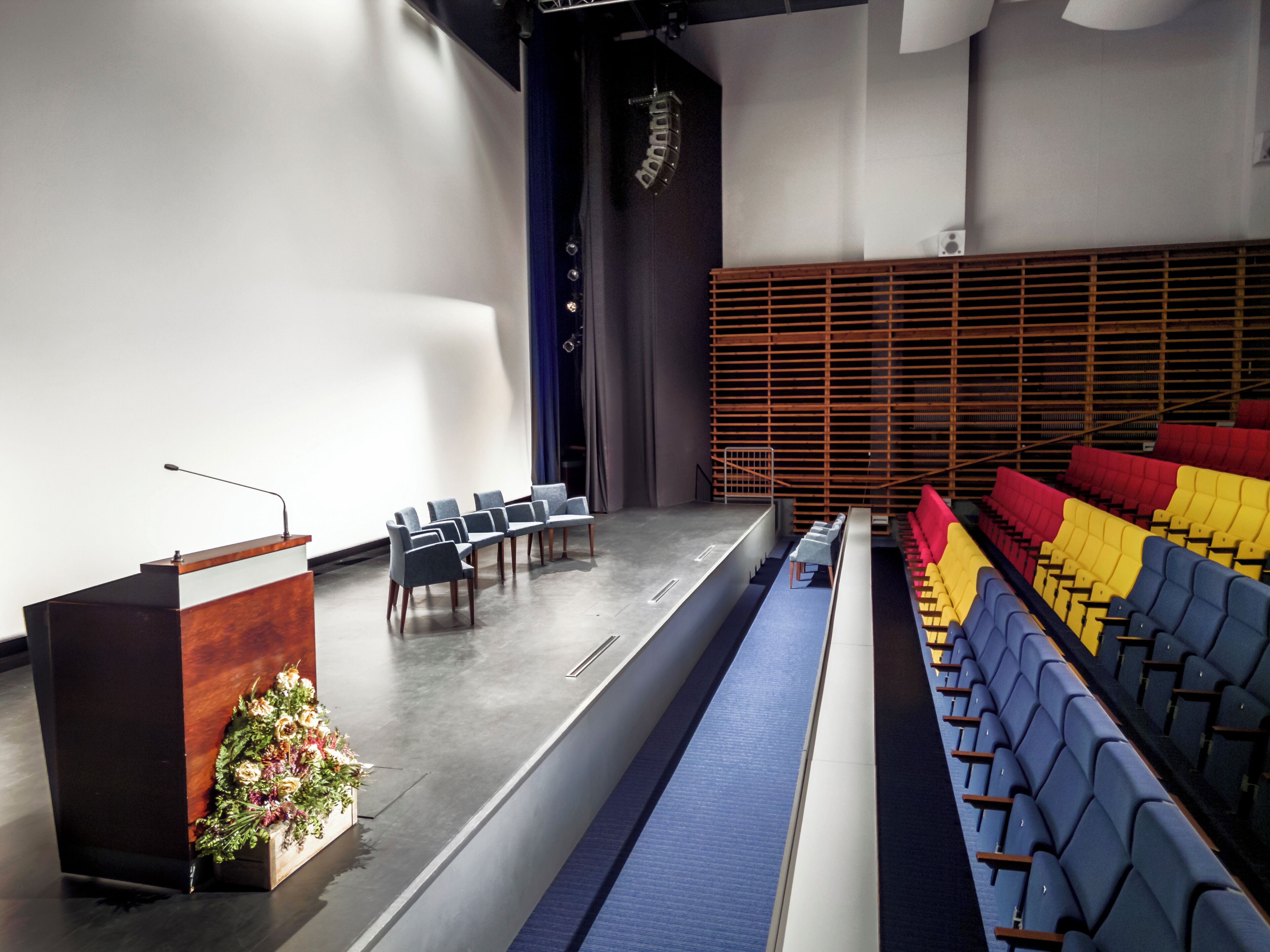 Un salón de conferencias con un atril, filas de sillas y un escenario.