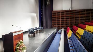 Un salón de conferencias con un atril, filas de sillas y un escenario.
