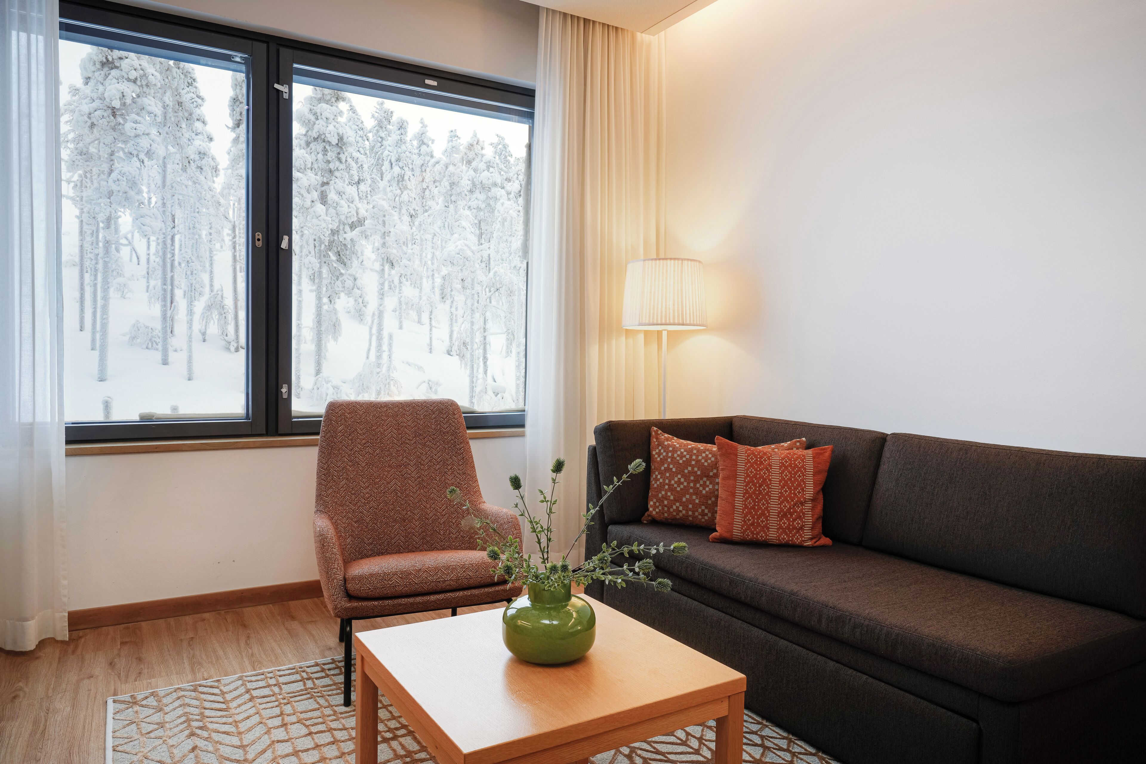 A cozy room with a sofa, armchair, and a table with a vase.