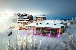Un hotel cubierto de nieve con varias construcciones, remontes y un paisaje nevado.