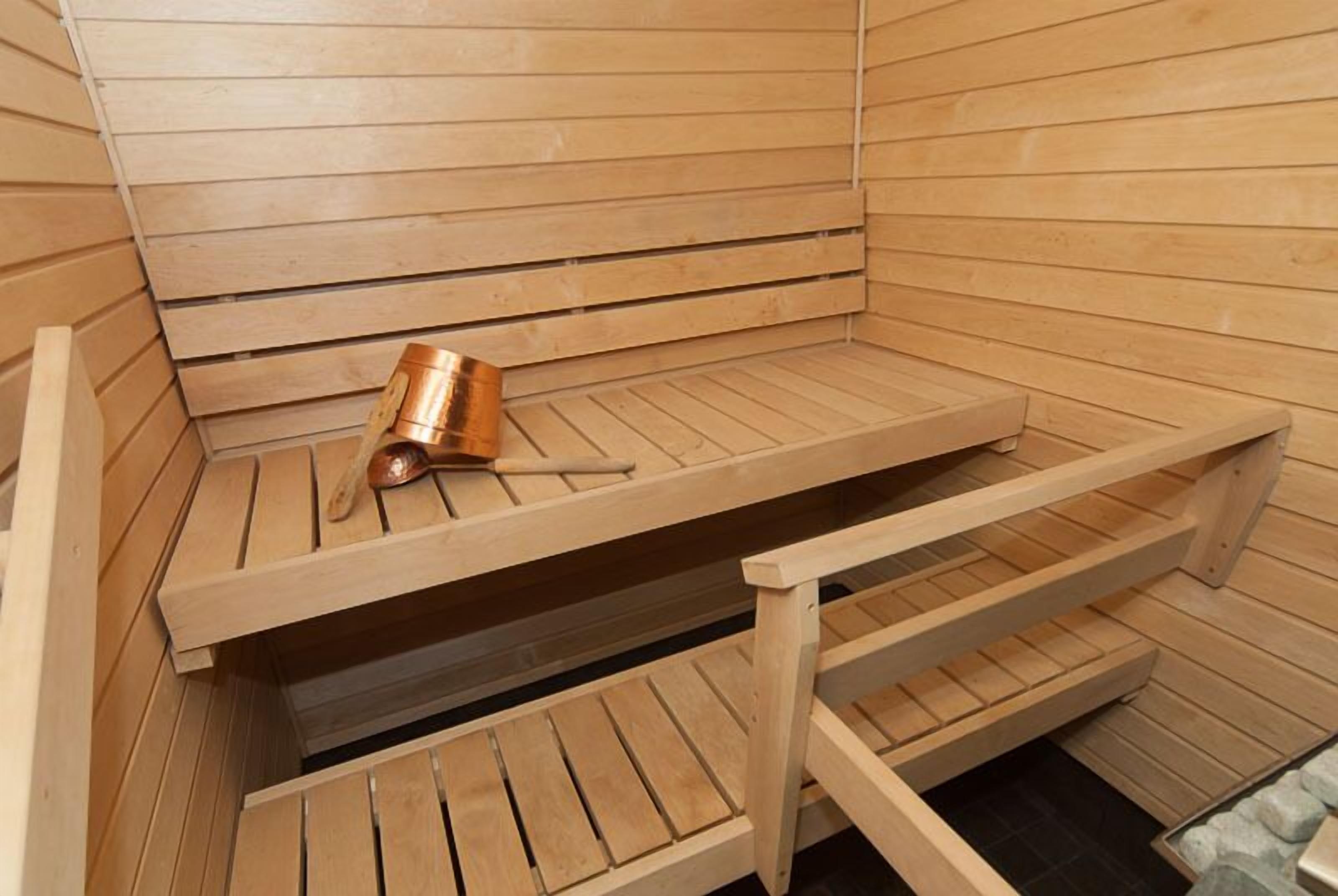 Un sauna avec des bancs en bois et un seau en cuivre.