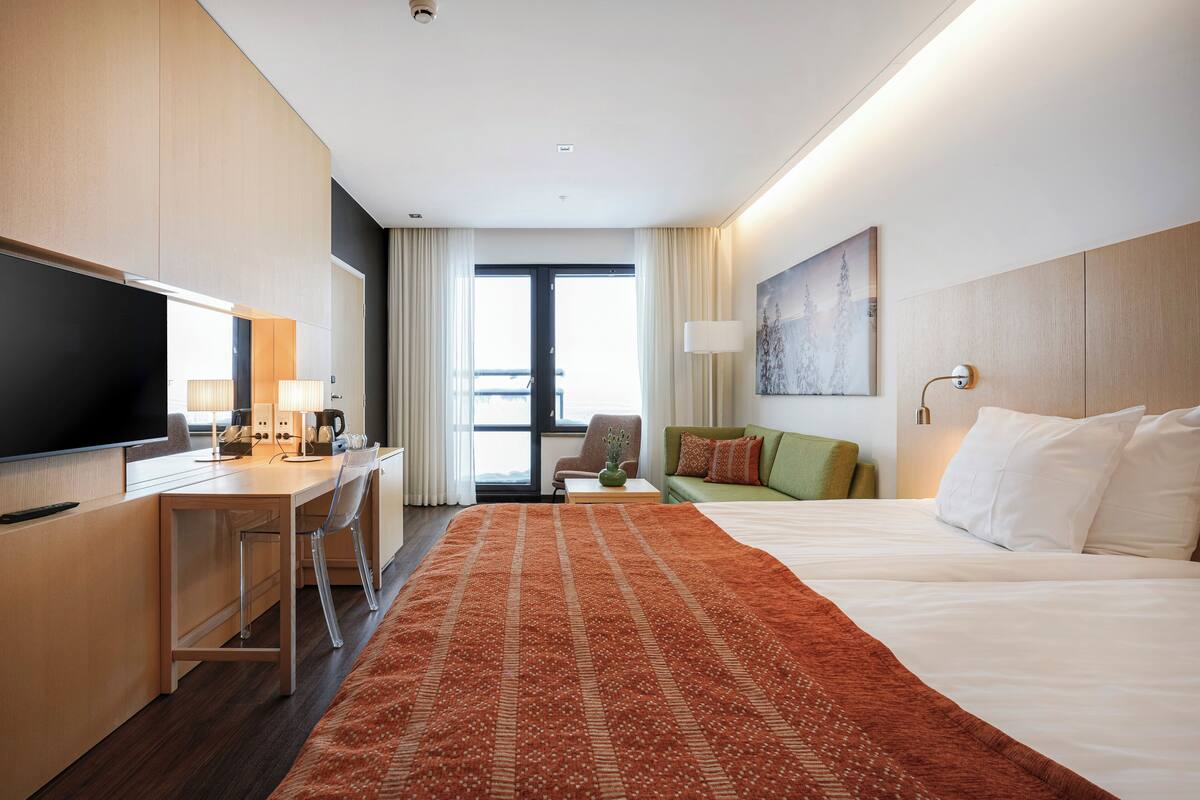 Una habitación de hotel con una cama, un escritorio, un televisor y una ventana con cortinas.