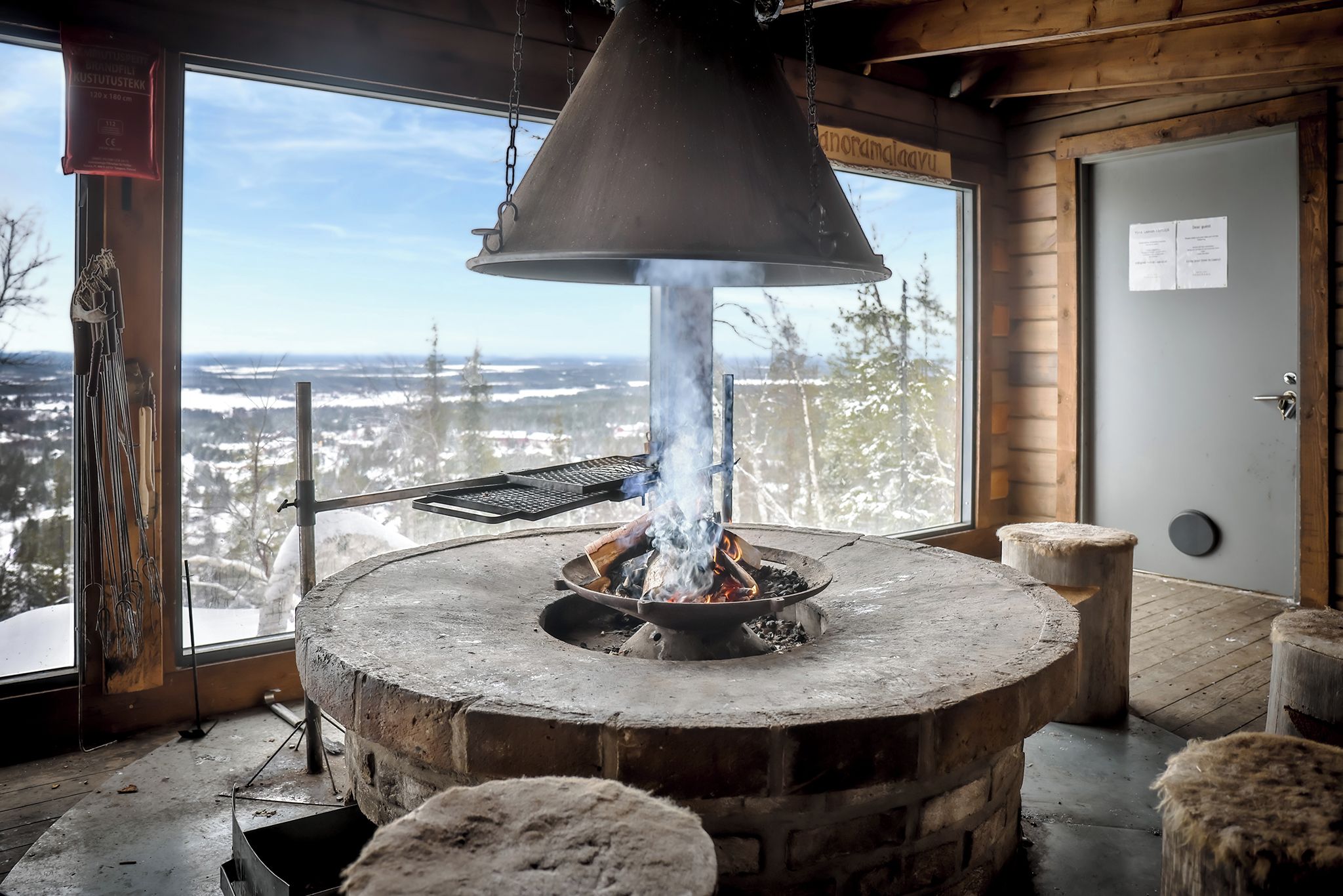 Una chimenea de piedra con un tiro, una ventana con vistas a un paisaje nevado y una puerta con un cartel.