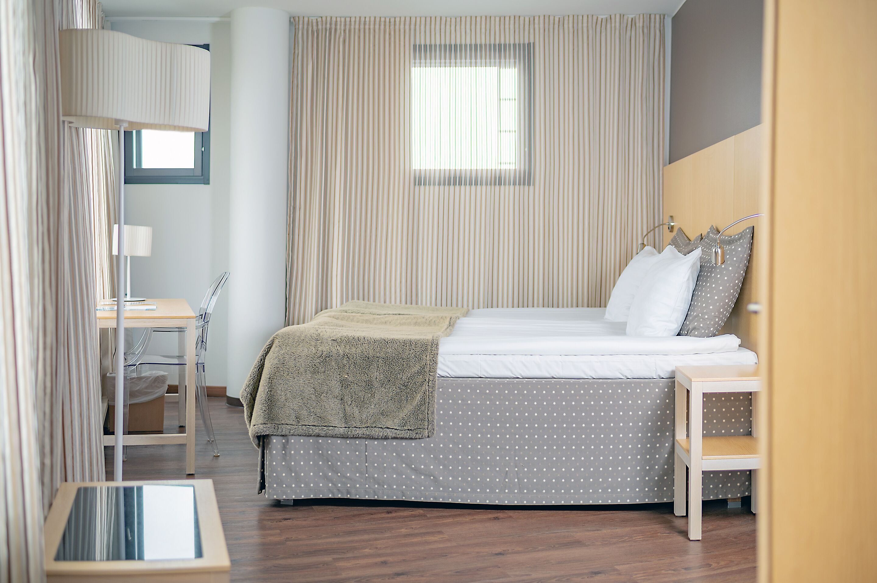 A neatly arranged bedroom with a bed, bedside table, and a desk with a chair.