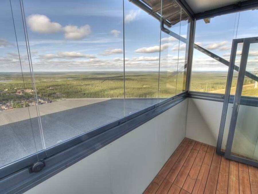 A balcony with a wooden floor and a glass wall offering a view of a rural landscape.