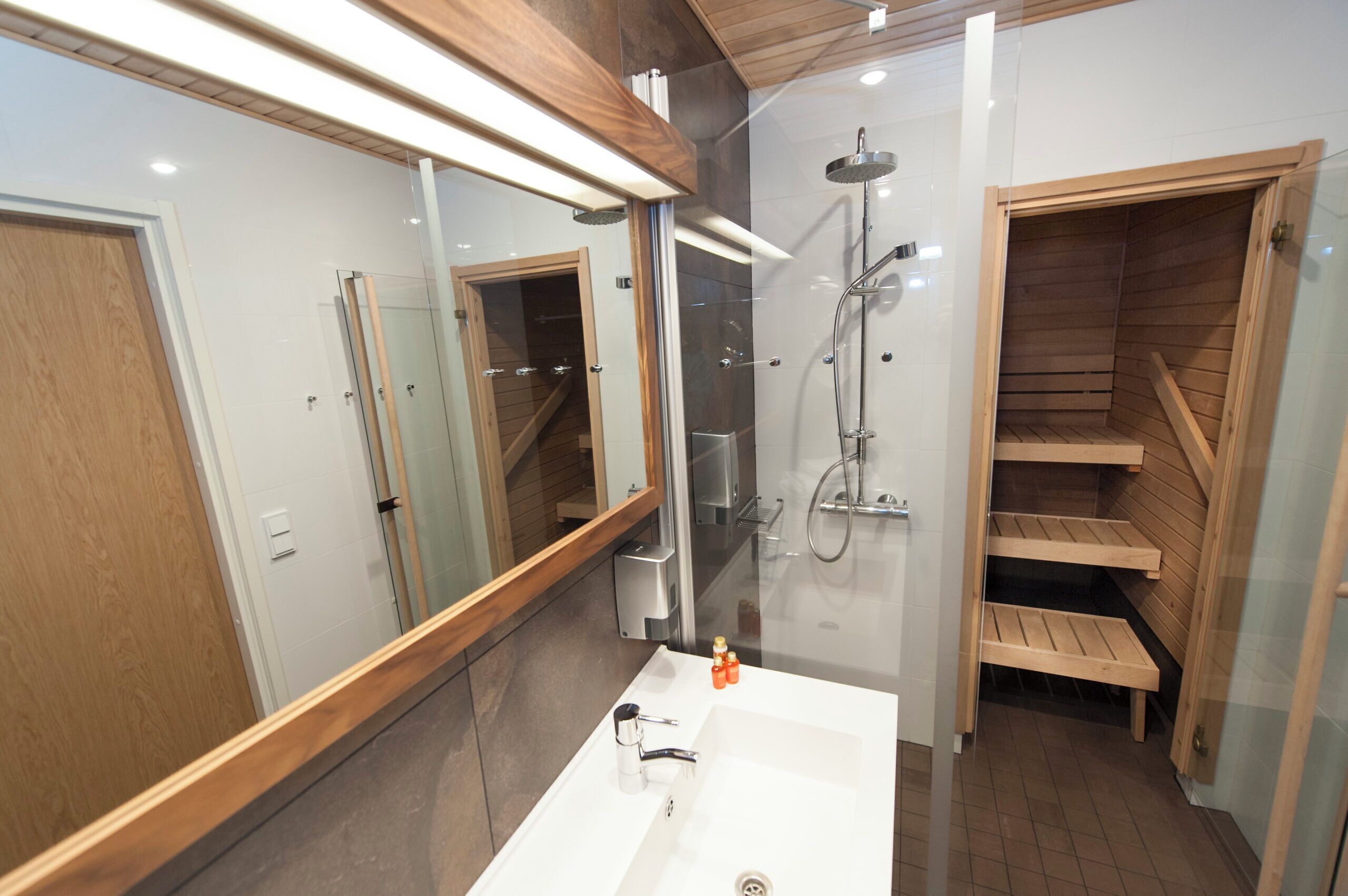 A modern bathroom with a large mirror, a white sink, a shower, and wooden shelves.