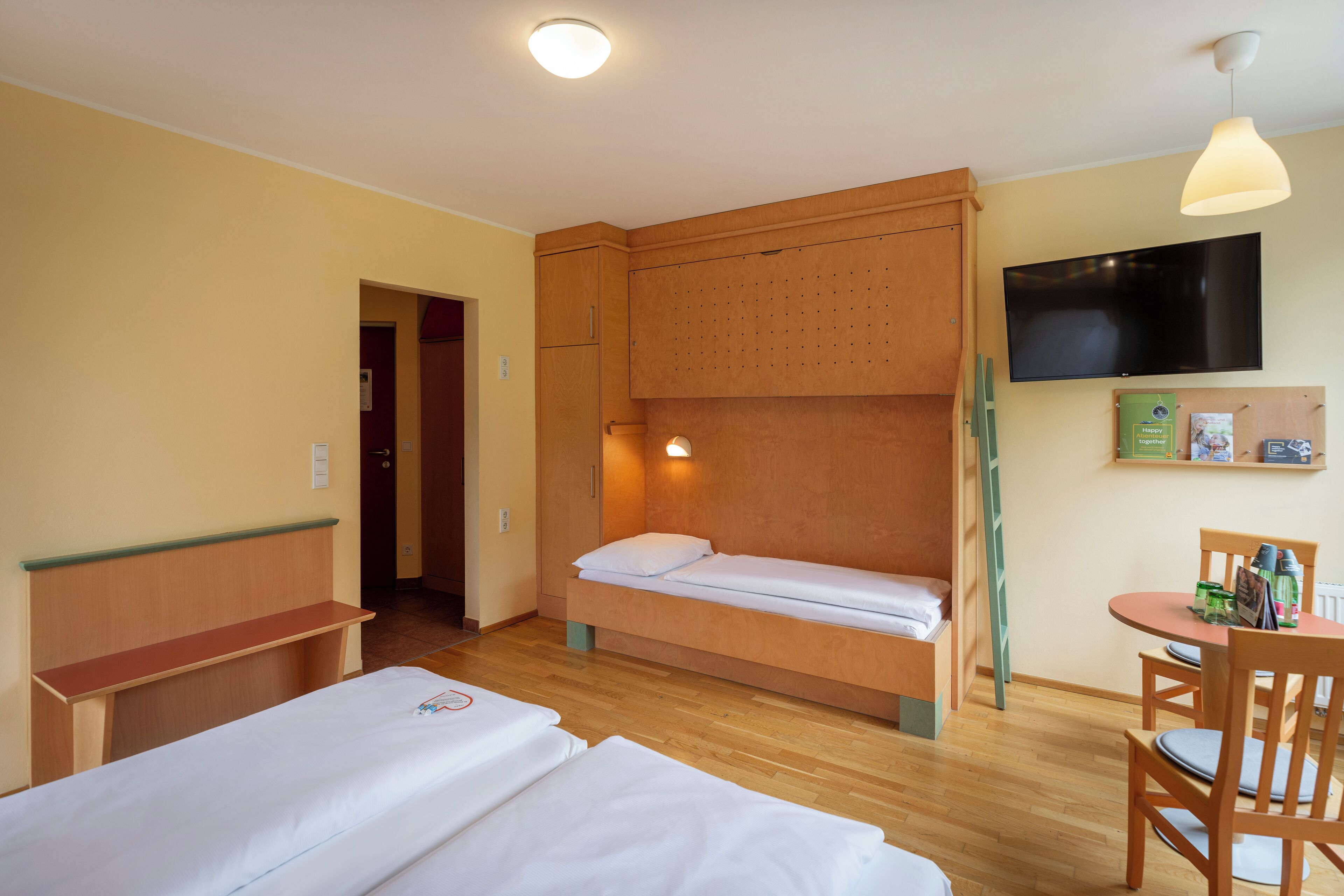 A room with two beds, a desk, a chair, a television, and a shelf with items.