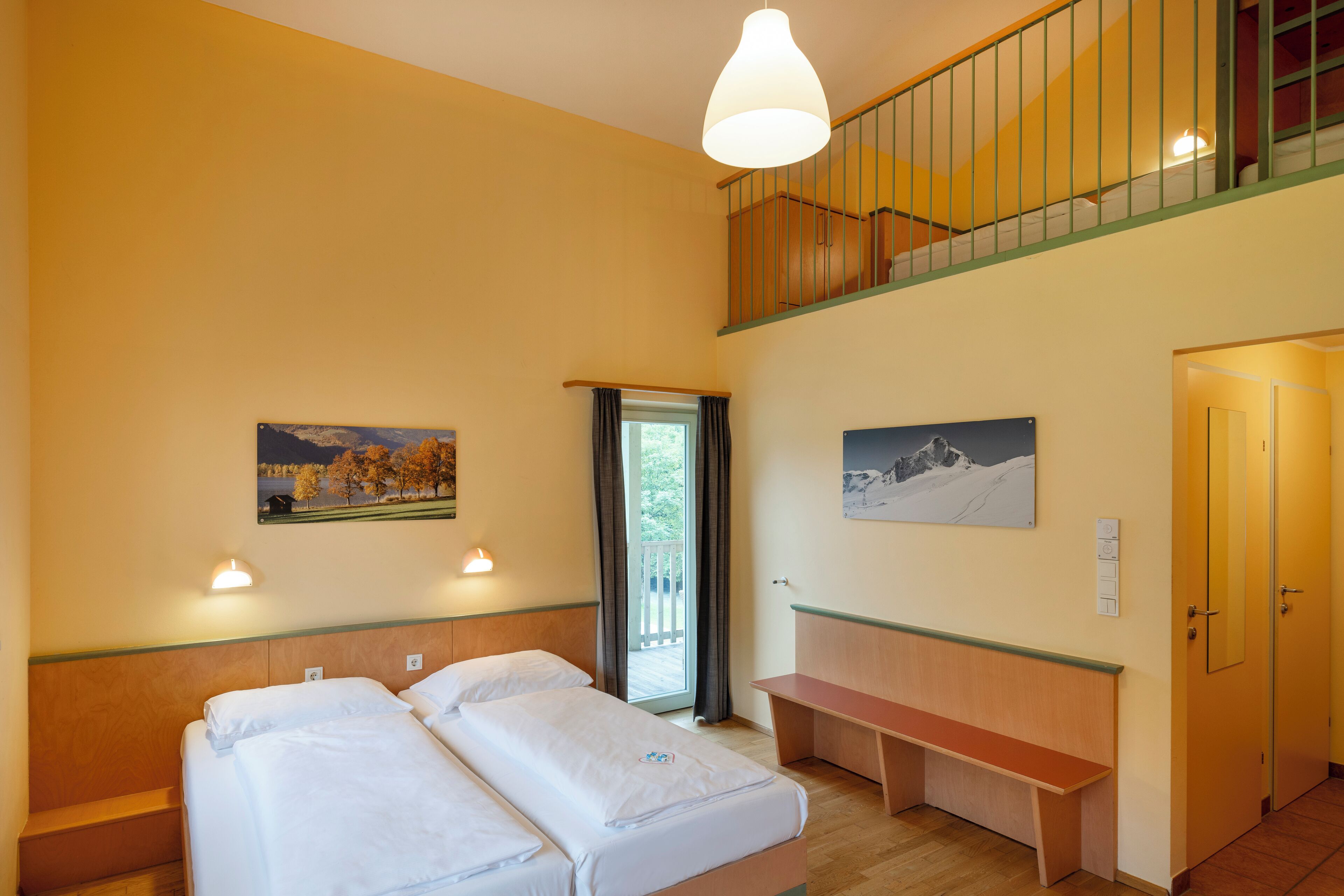 Habitación de hotel con dos camas, una banca, un balcón y pinturas en las paredes.