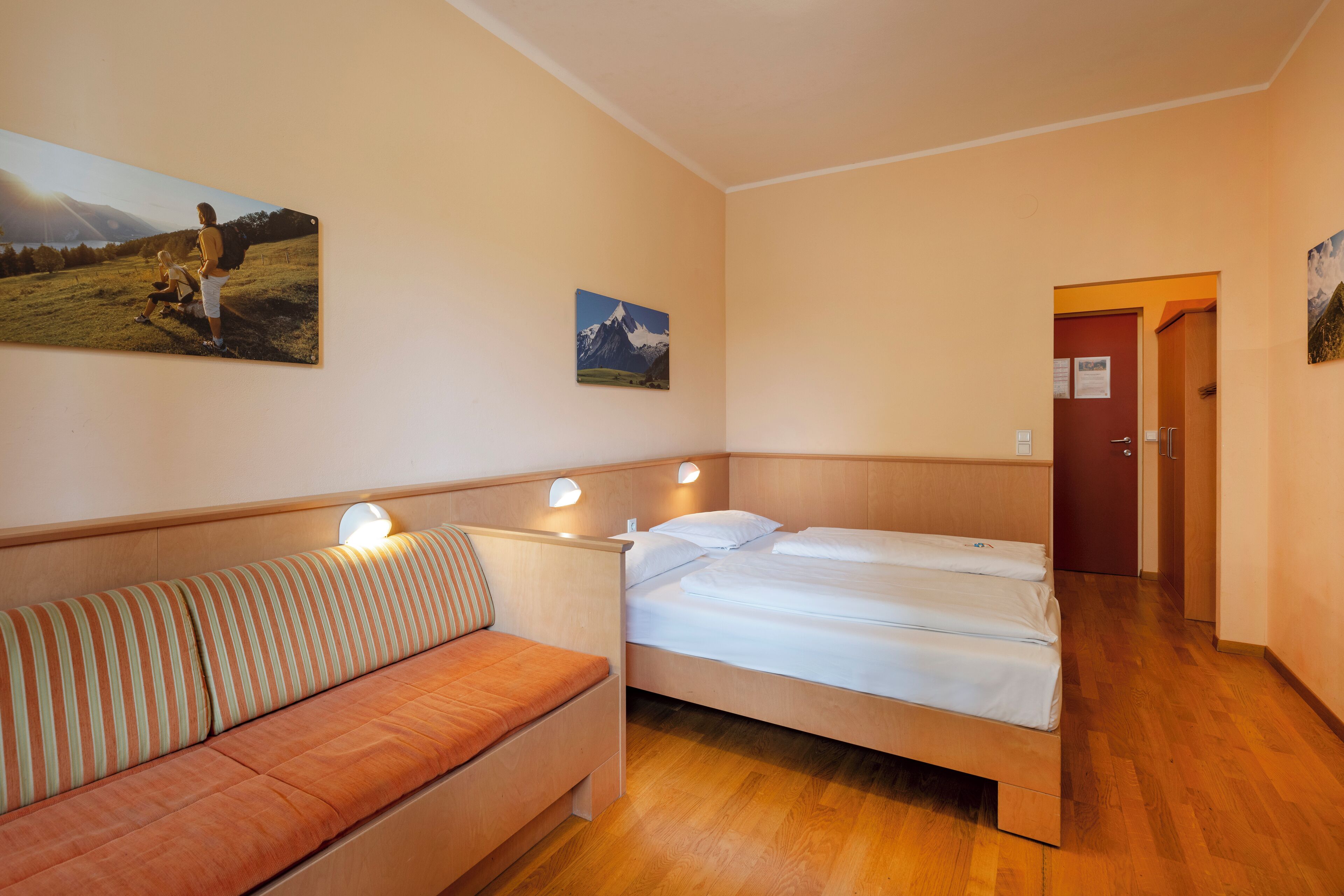A room with a bed, a sofa, and two wall-mounted lamps.