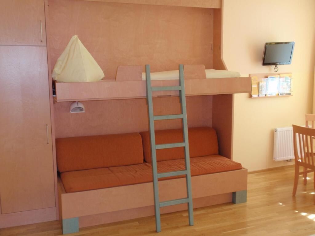A bunk bed with a ladder, a sofa, a television on the wall, and a chair.