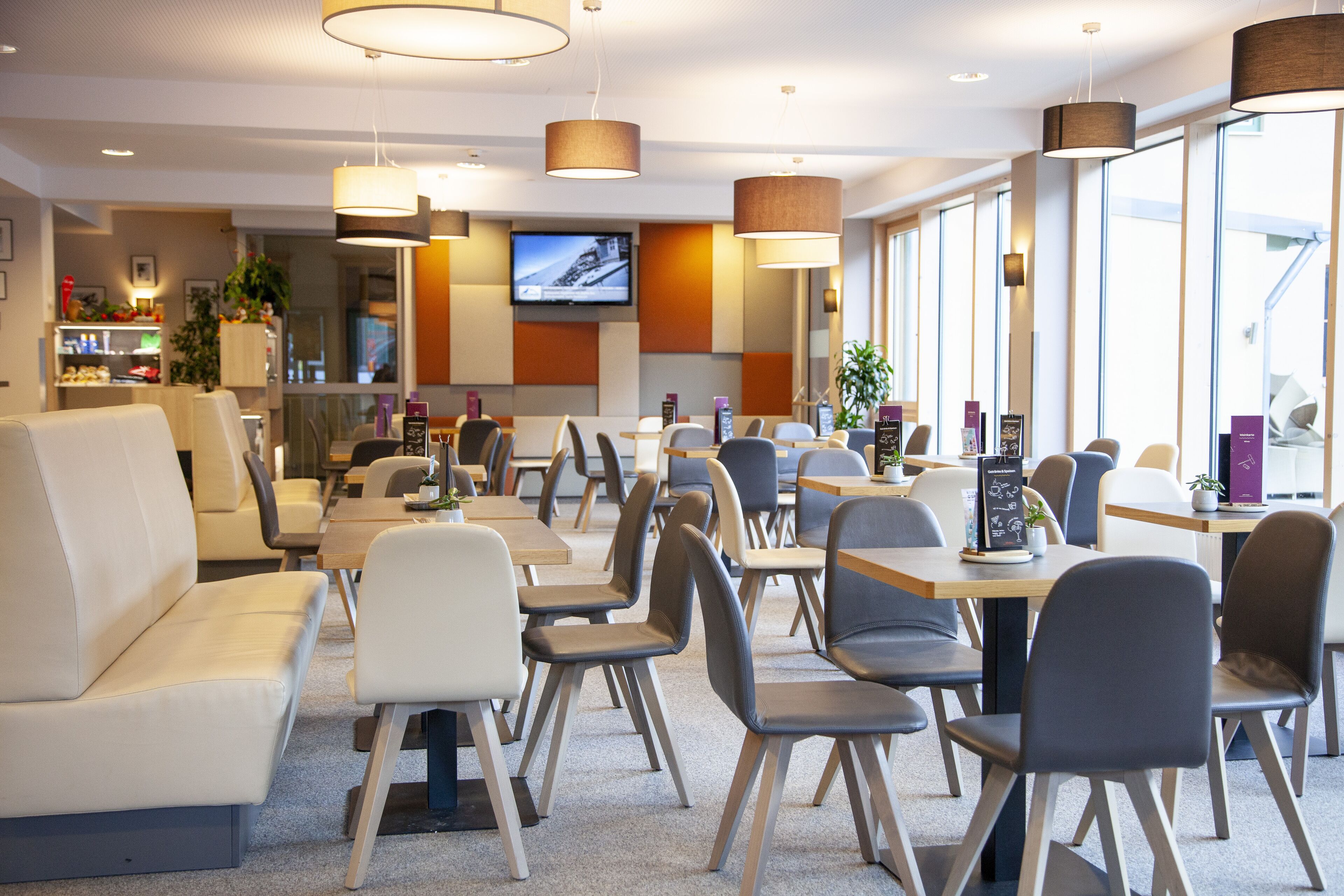 Un restaurante moderno con varias áreas de comedor, incluyendo mesas y sillas, y una pantalla de televisión montada en la pared.