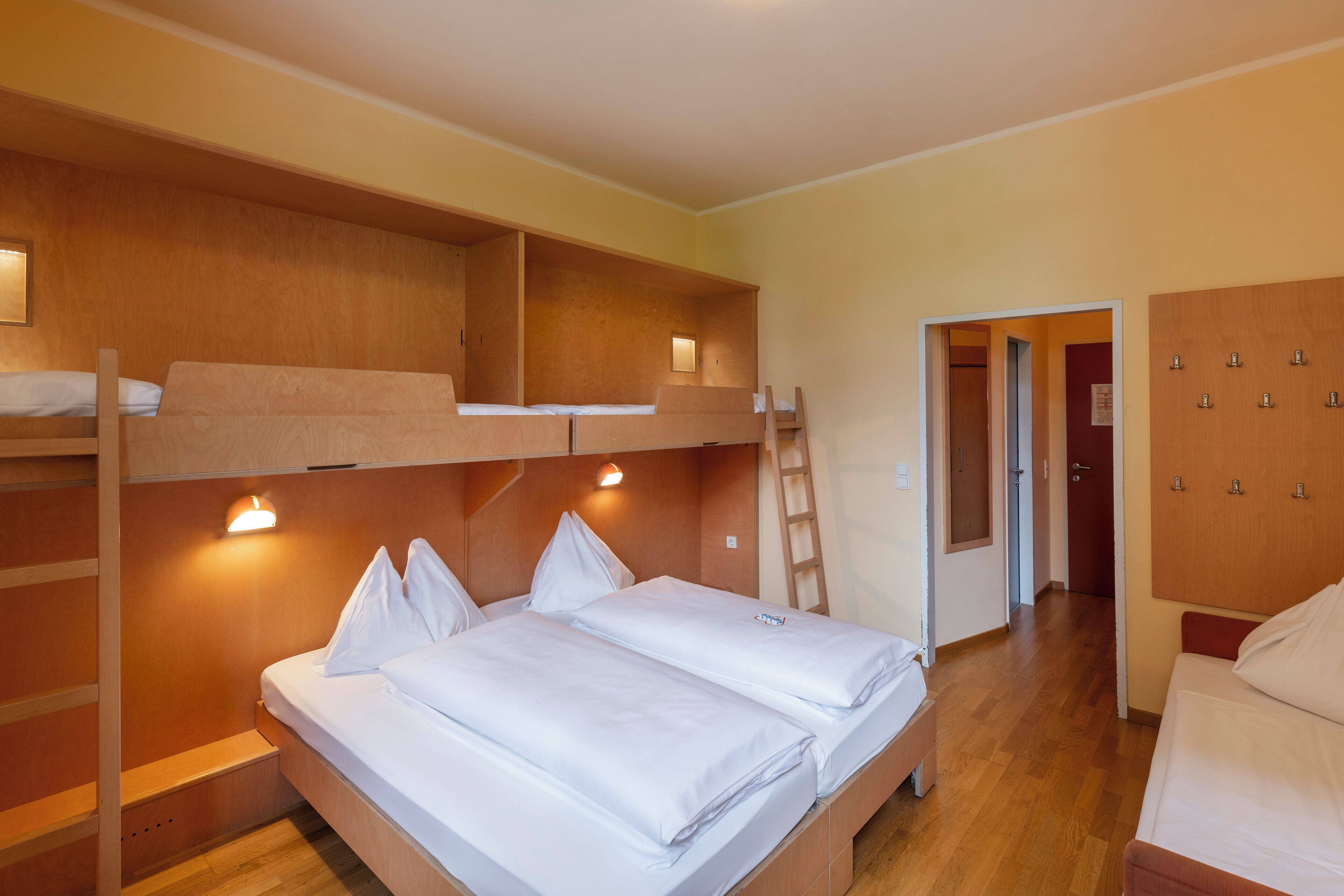 Dormitorio con literas, una escalera de madera, un escritorio y un armario.
