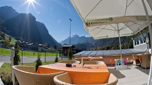Restaurante com mesas ao ar livre, vista para a montanha e um grande guarda-sol.