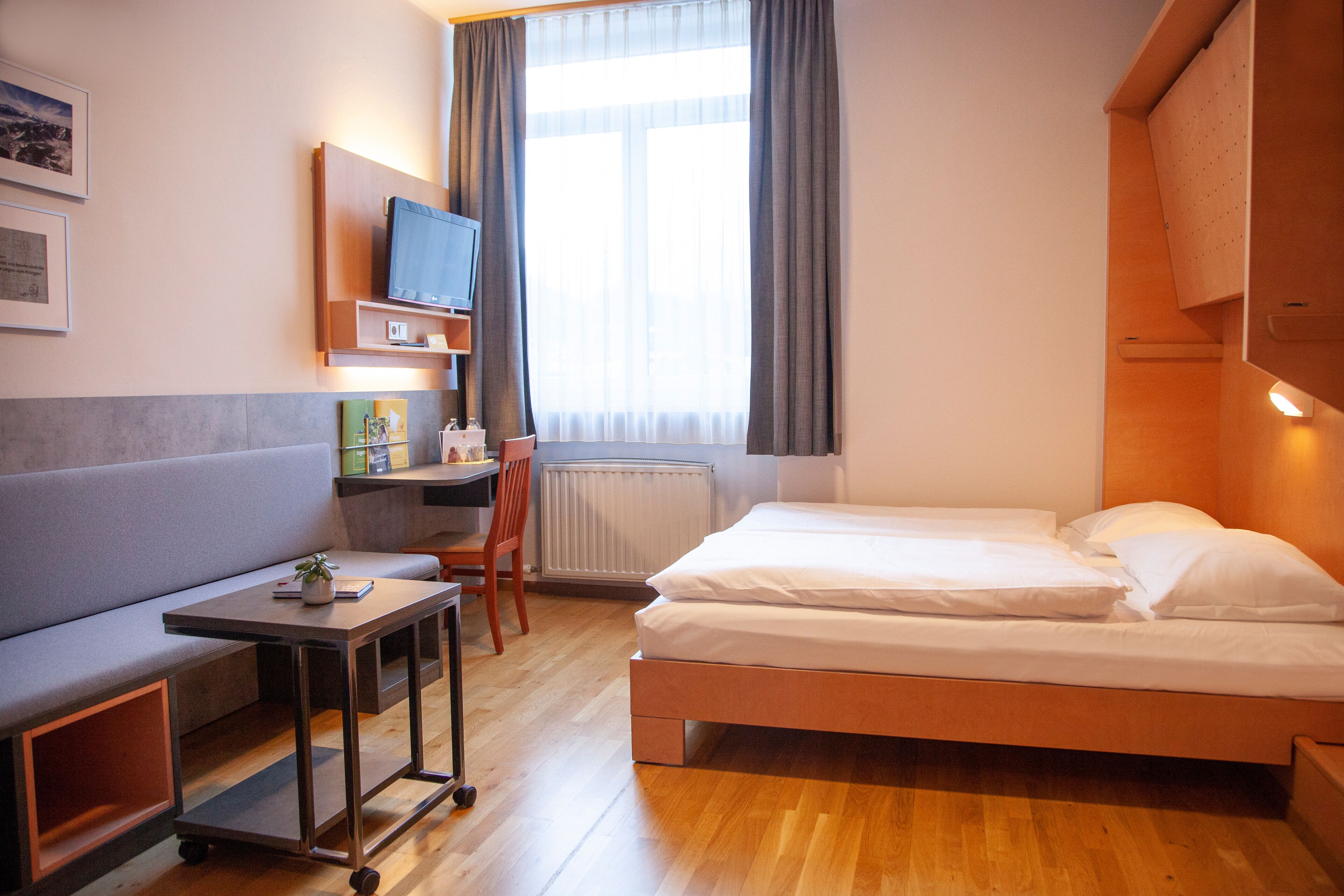 A compact hotel room with a bed, a desk, a chair, and a small table.