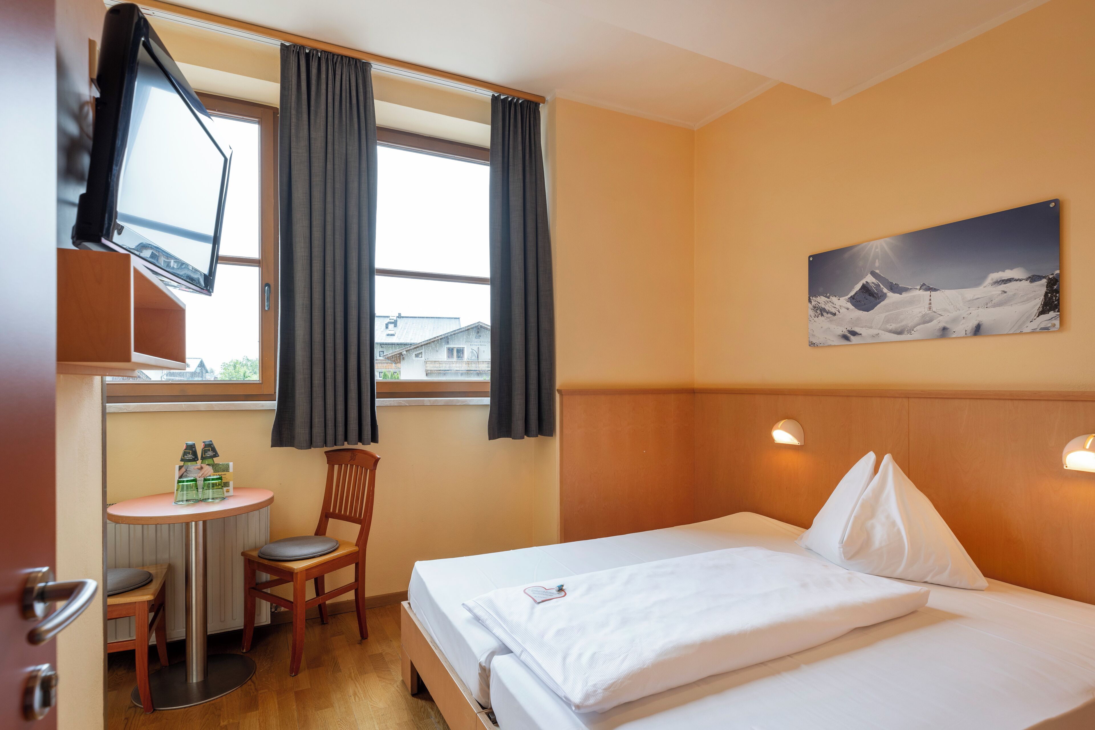 A hotel room with a bed, a desk, a chair, a TV, and a window with curtains.