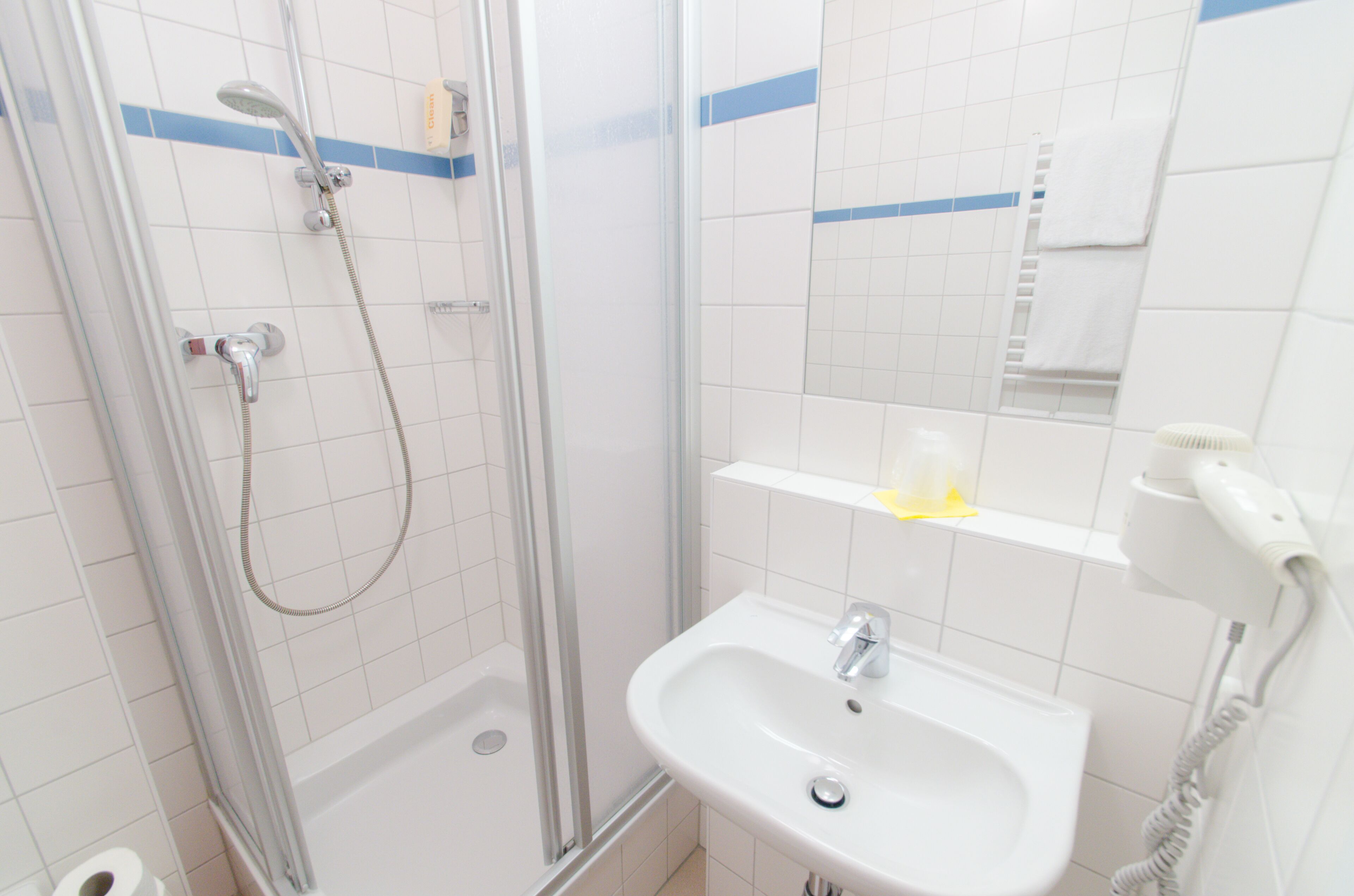 A bathroom with a glass-enclosed shower, a sink, a towel rack, and a hairdryer.