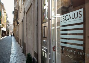 A narrow street with a building featuring a sign for 'ESCALUS' and a glass door with a sign for 'Verona Luxury Suites'. - Escalus Luxury Suites Verona (Verona)