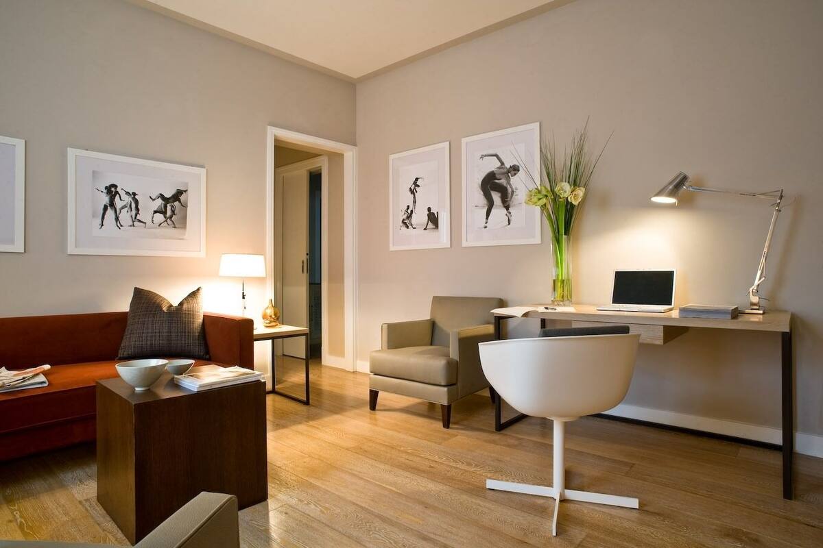 A modern living room with a sofa, coffee table, and a desk with a laptop. There are framed pictures on the wall and a vase with flowers on the desk.