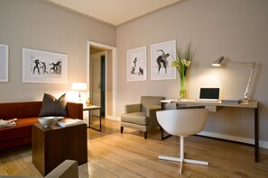 A modern living room with a sofa, coffee table, and a desk with a laptop. There are framed pictures on the wall and a vase with flowers on the desk. - Escalus Luxury Suites Verona (Verona)