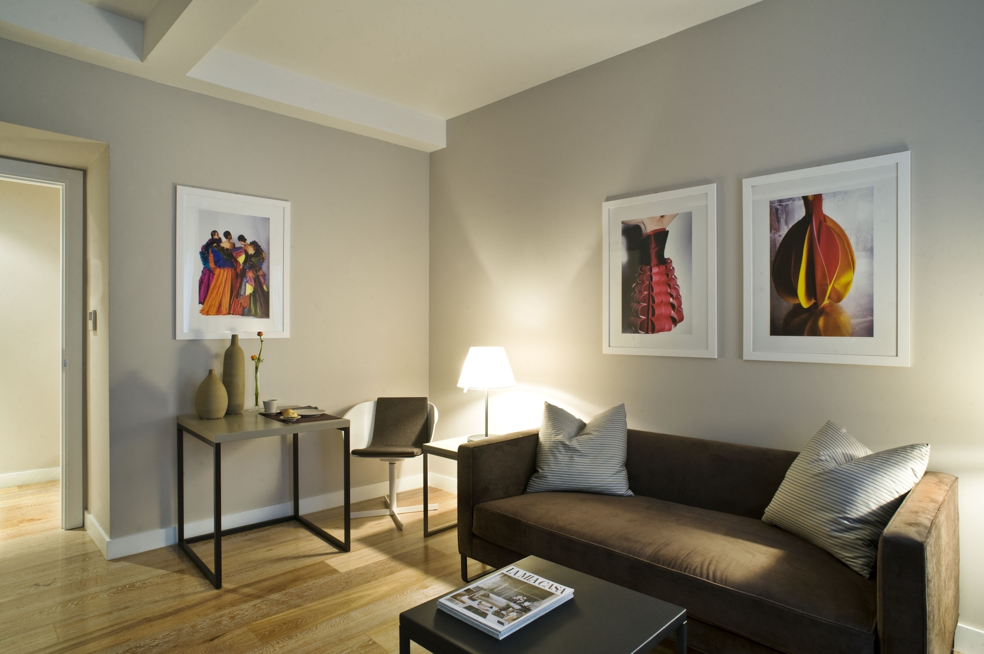 A modern living room with a brown sofa, a coffee table, a side table, a chair, and two framed artworks on the wall.