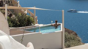 A pool with a view of the sea and mountains, a boat in the water, and a person relaxing.