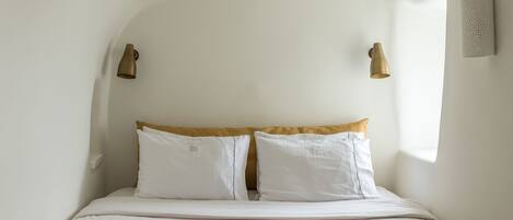 A bed with white bedding and a beige headboard, two wall-mounted light fixtures, and a textured wall panel.