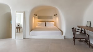 A minimalist bedroom with a bed centered under a sloped ceiling, a wooden chair, and a small table.
