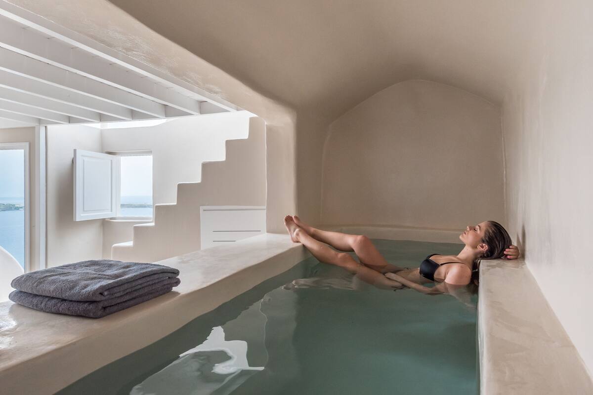 Una persona relaxant-se en una zona de piscina petita i privada amb vista al mar, una escala i una tovallola sobre una superfície elevada.