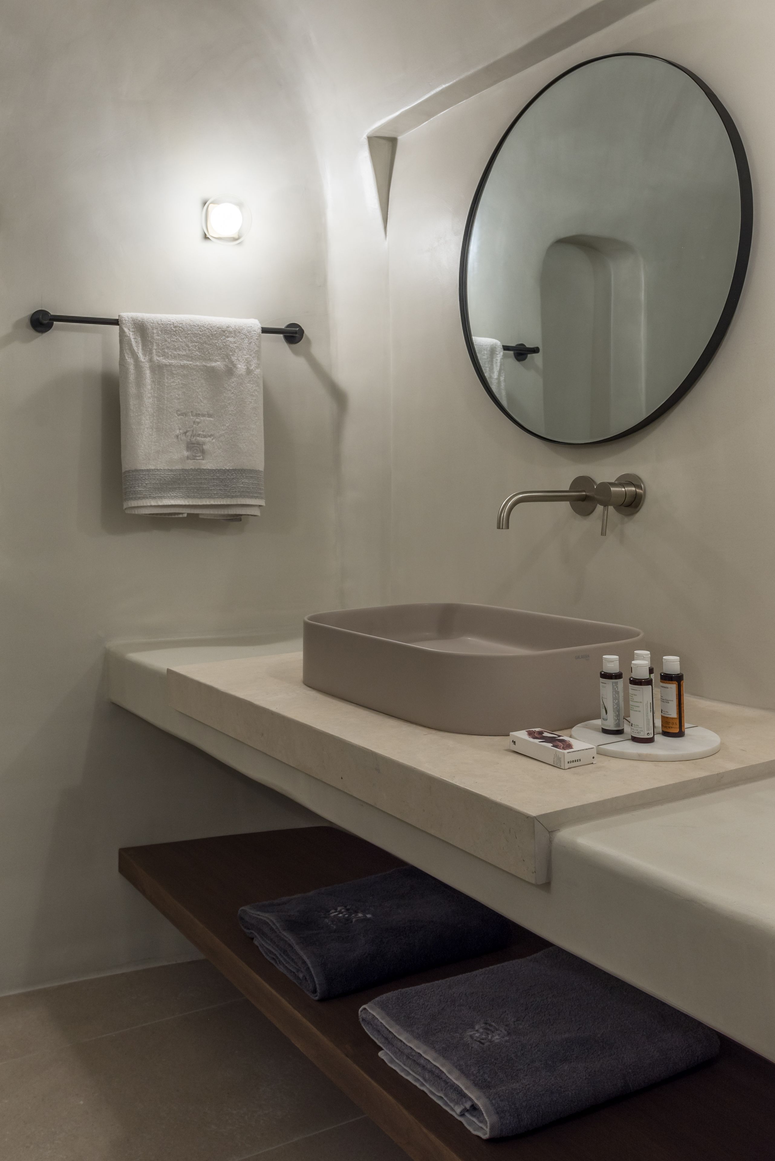 A modern bathroom with a beige sink, a round mirror, and a towel rack.