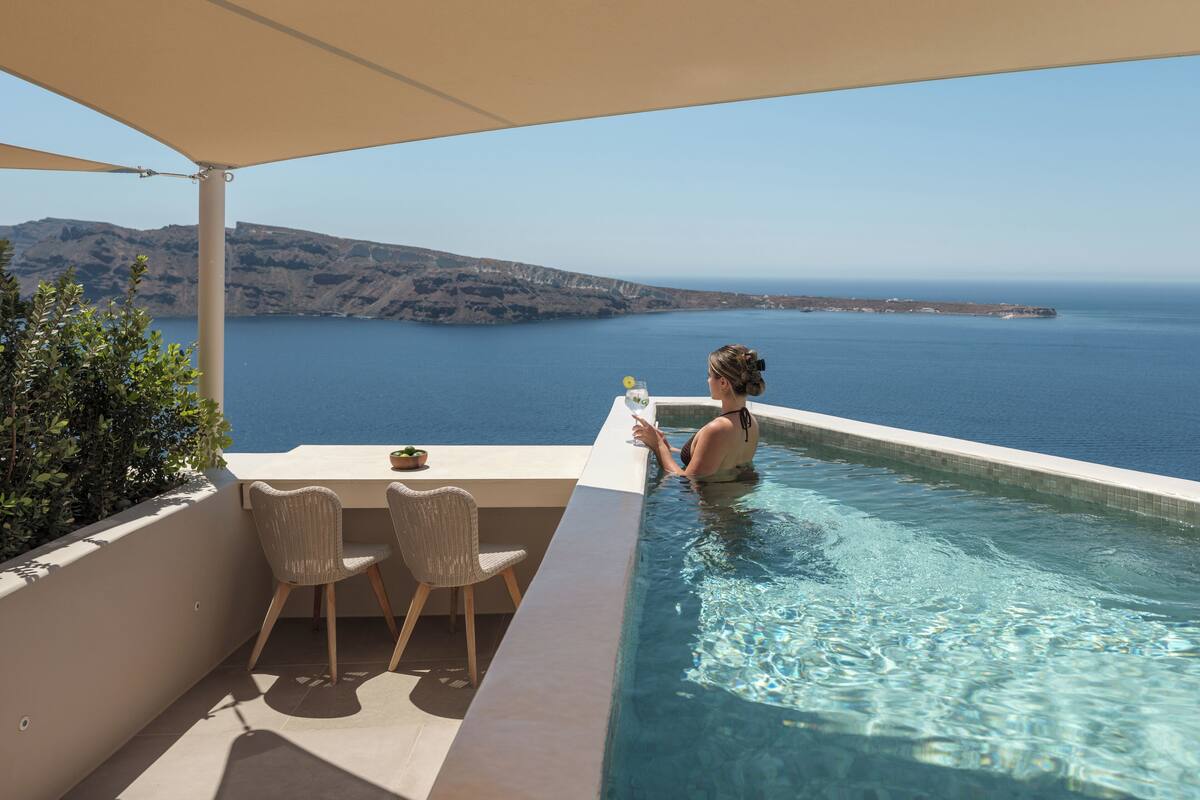 Una piscina amb vista al mar, una taula amb cadires i una planta en test.