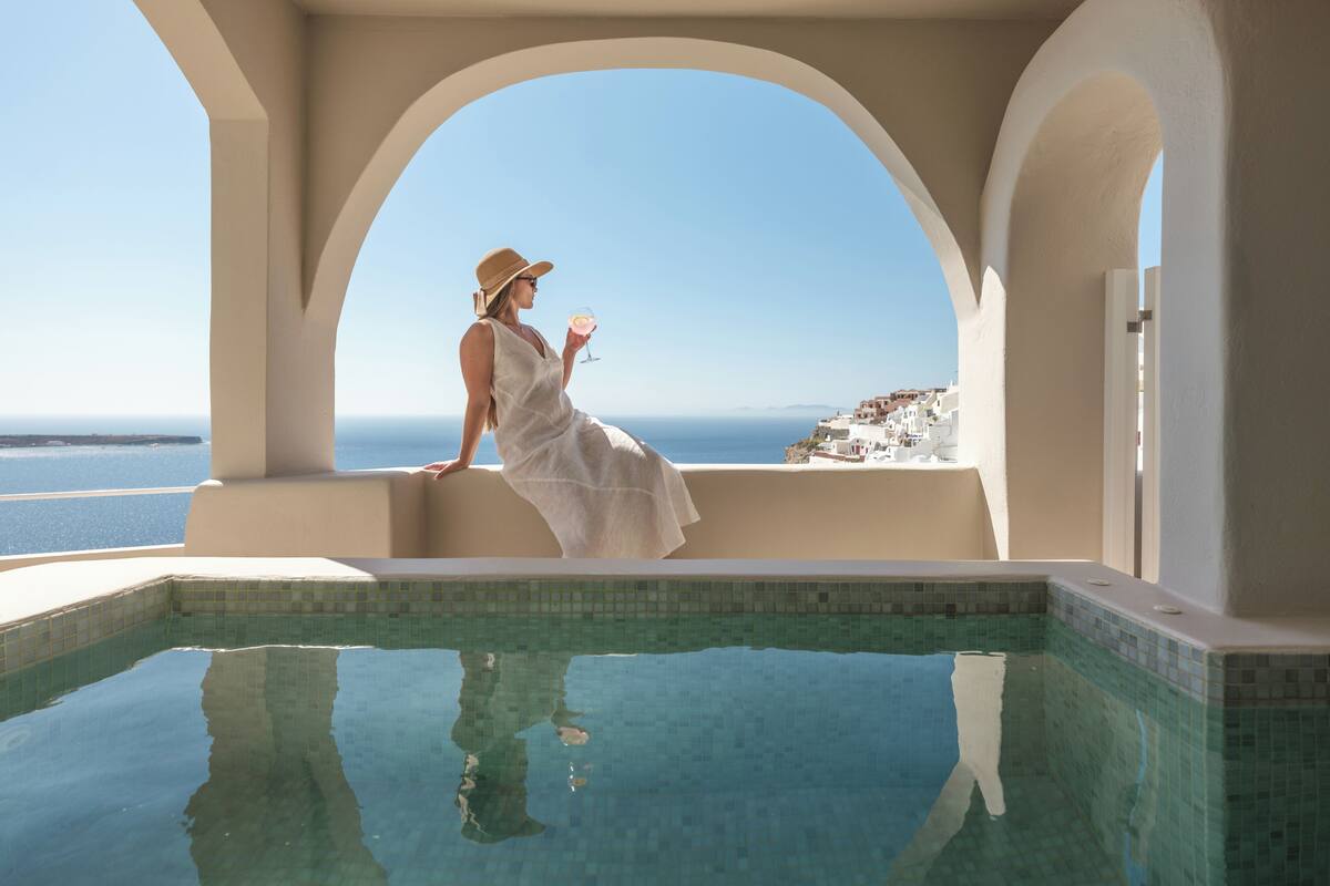 Una dona amb un vestit blanc a la piscina, amb vistes al mar i edificis blancs.