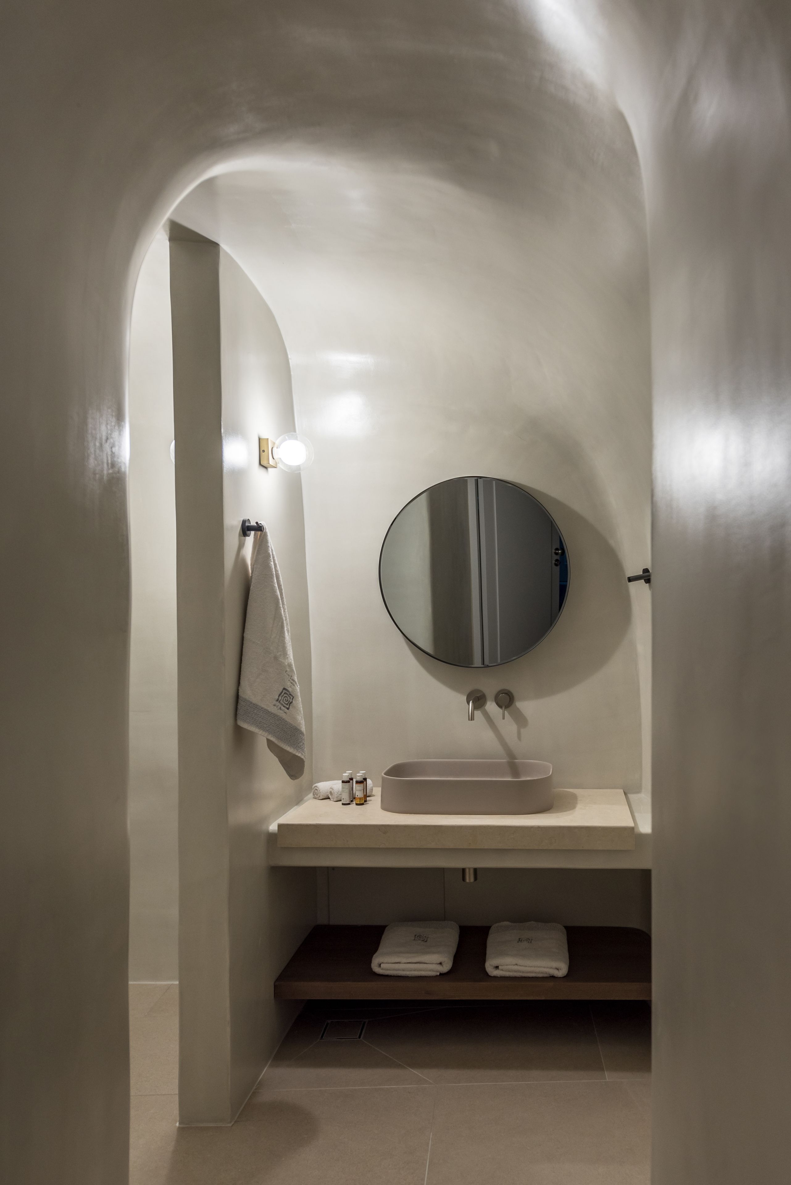 Une salle de bain moderne avec un miroir rond, un porte-serviettes et un lavabo.