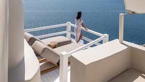 A balcony with white furniture, a person in a white dress, and a view of the sea and distant land.