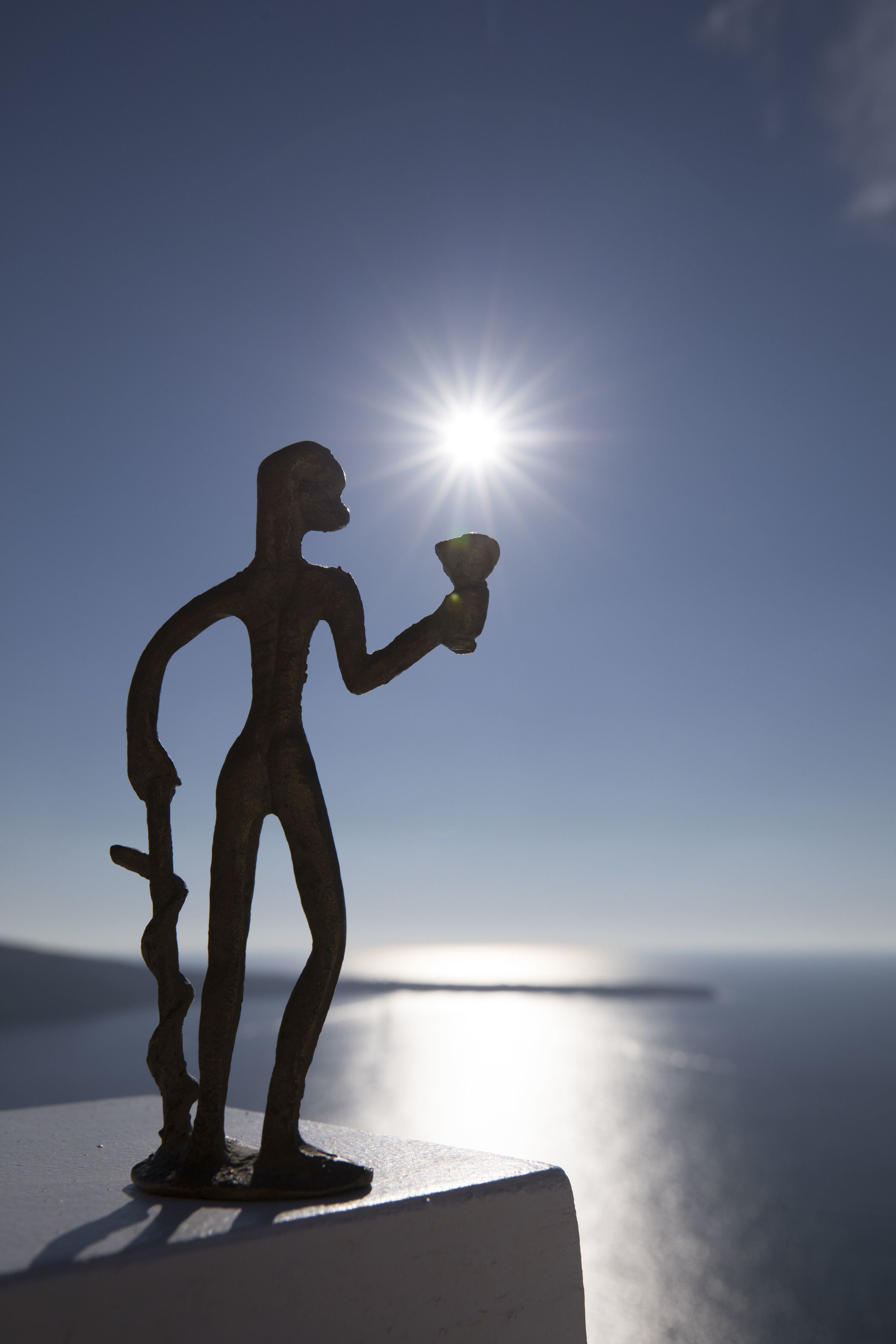 La silhouette d’une personne tenant une torche devant un soleil éclatant, avec une mer calme en arrière-plan.