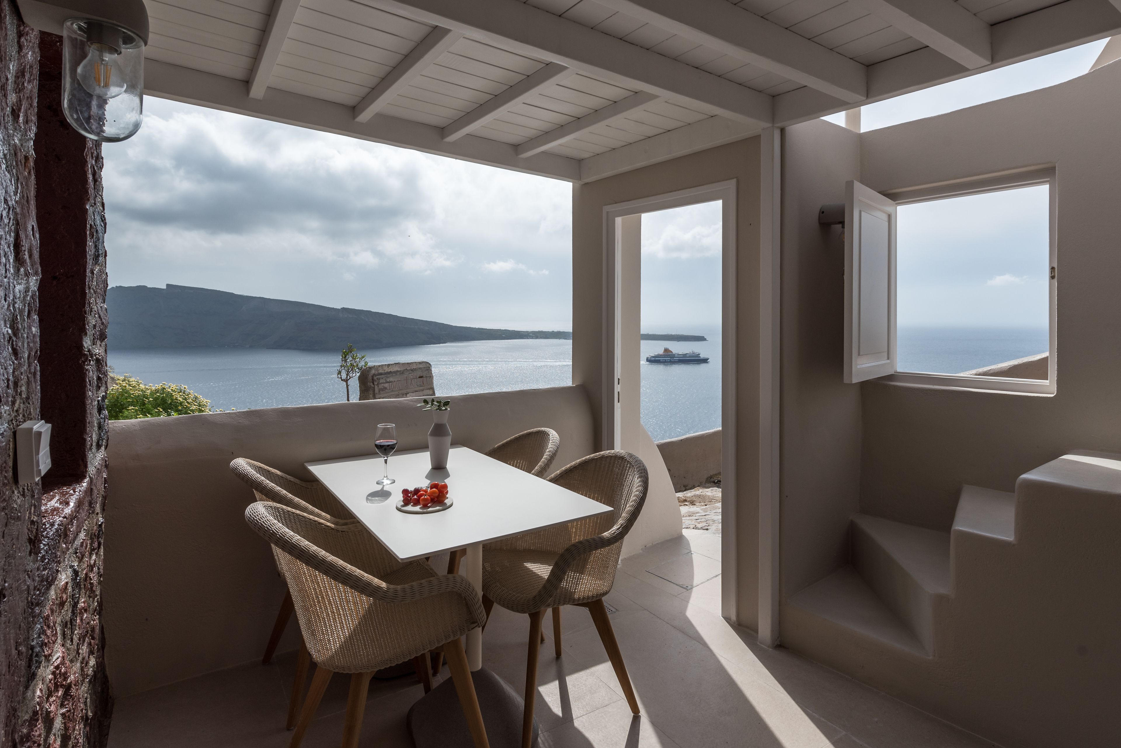 A balcony with a table and chairs, overlooking a body of water and a distant island.