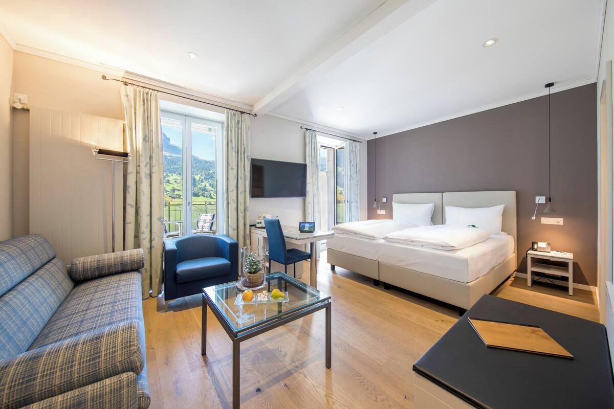 Quarto de hotel moderno com cama, sofá, escrivaninha e vista para o exterior.