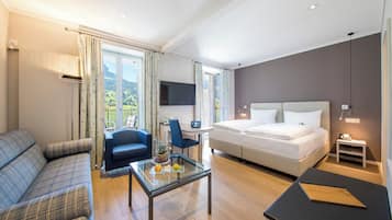 A modern hotel room with a bed, a sofa, a desk, and a view of the outdoors.