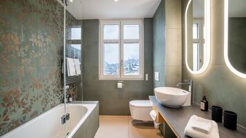 A modern bathroom with a bathtub, toilet, and sink. There is a window providing a view of the cityscape.