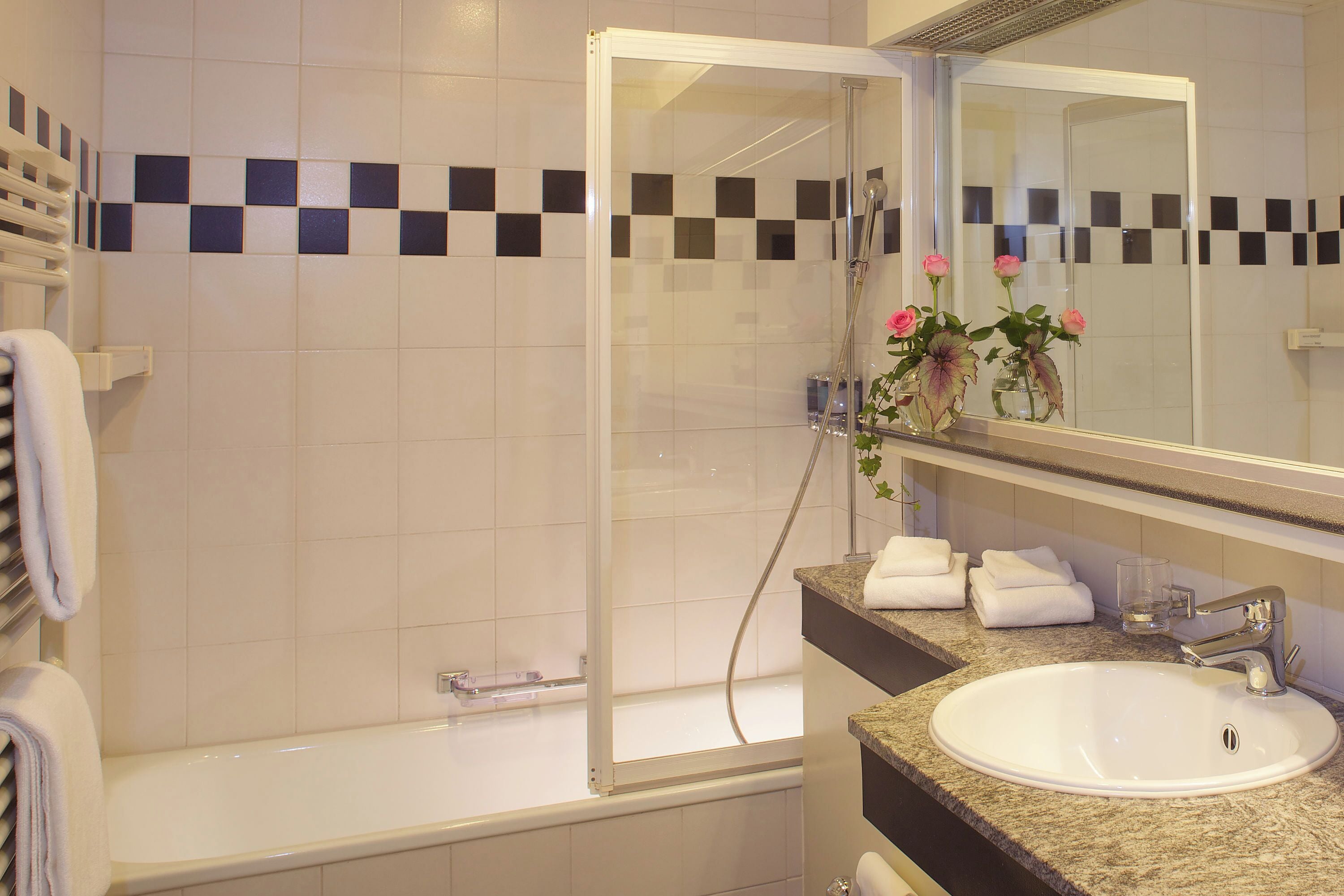 A bathroom with a bathtub, a sink, and a shower. There are towels and a vase with flowers on the counter.