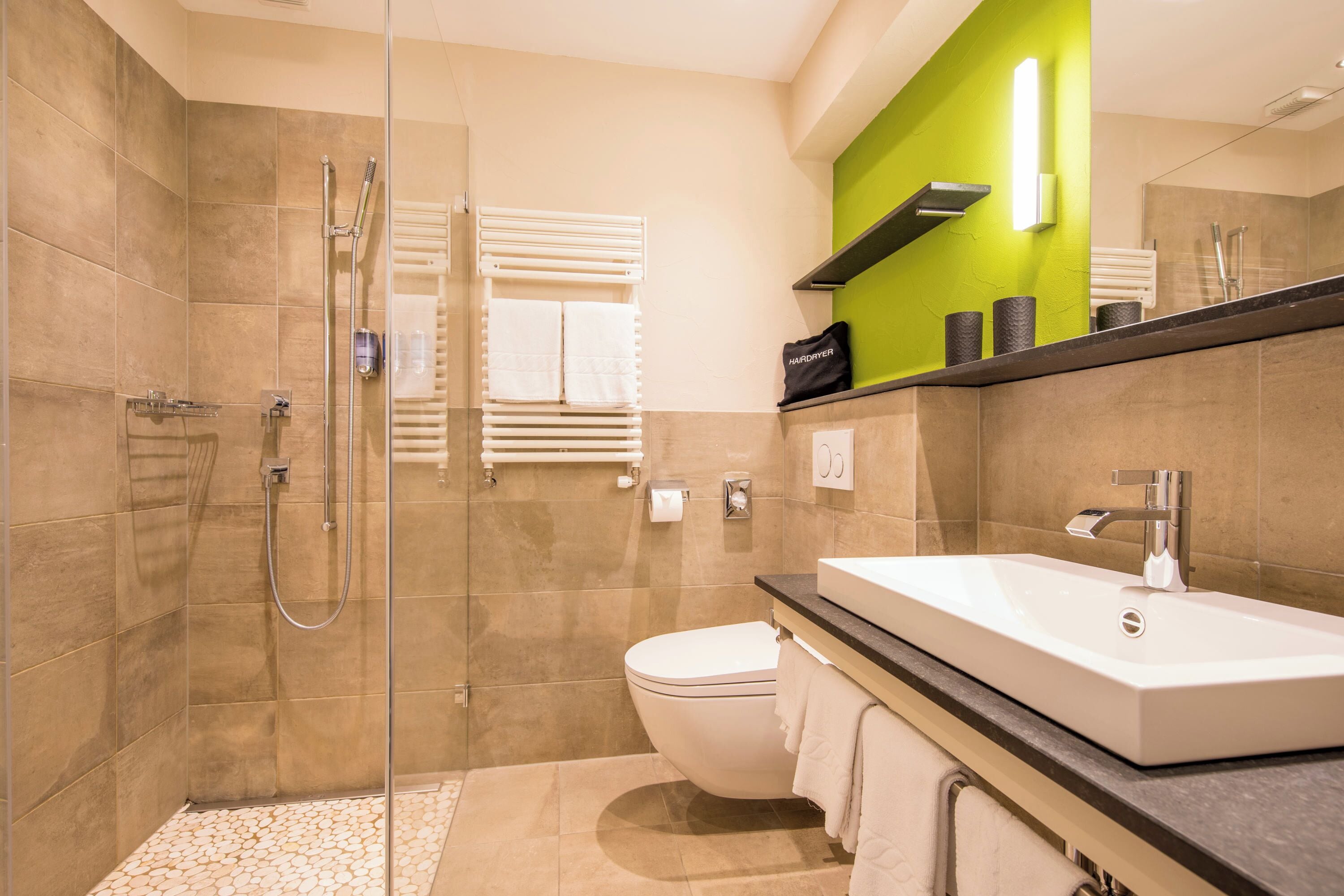 A modern bathroom with a glass-enclosed shower, a white sink, and a green accent wall.