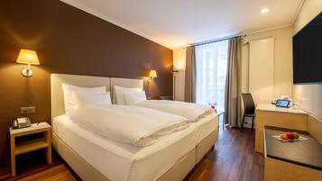 A hotel room with a large bed, bedside lamps, a desk with a computer, and a TV.