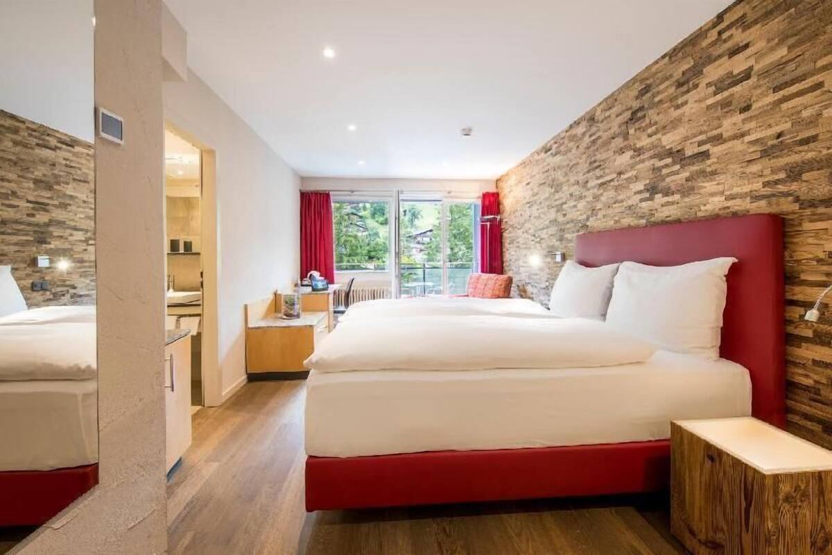 Quarto de hotel moderno com uma cama grande, uma parede de destaque em madeira e vista para o exterior.