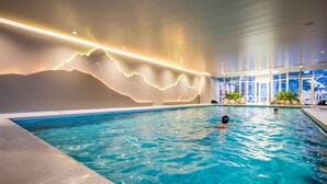 Una piscina interna con un murale raffigurante montagne e vista su un paesaggio innevato attraverso ampie finestre.